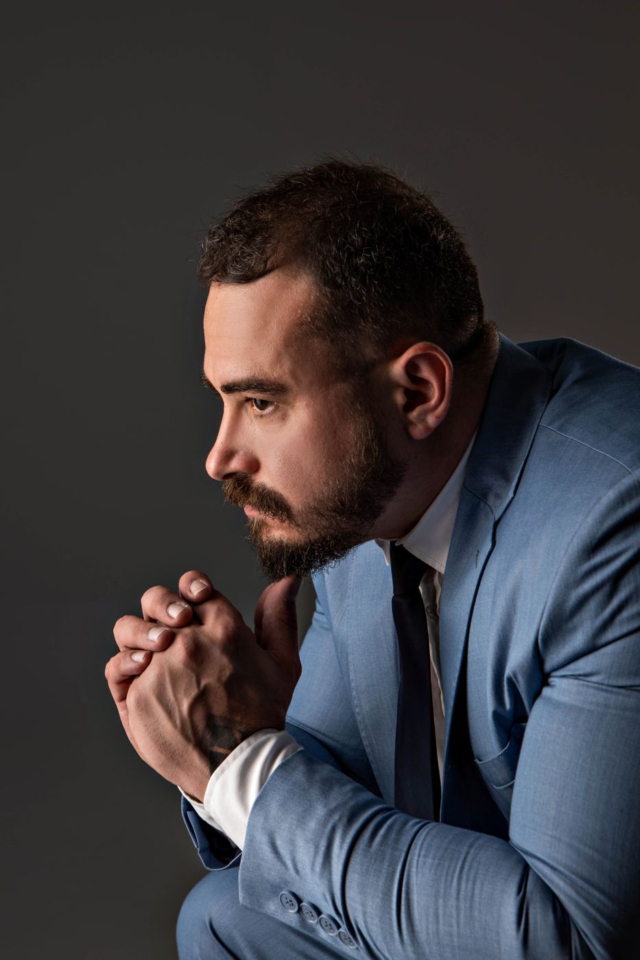 Pablo Dietrich de perfil, mãos unidas, em fundo escuro