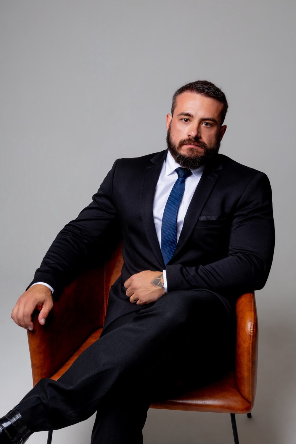 Pablo Dietrich sentado em poltrona de couro, de terno escuro e gravata azul